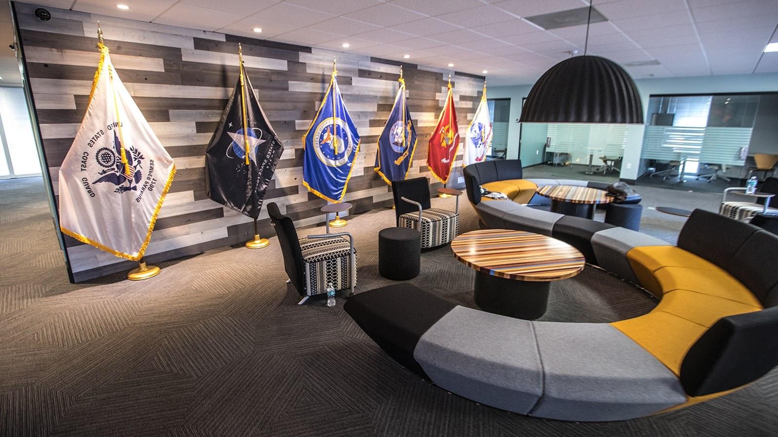 满帆军校学生成功中心的一张图片显示了一张大沙发, 小型会议室, 以及代表美国各军种的旗帜.